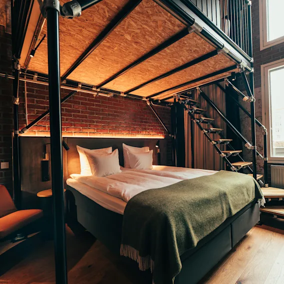 Tyylikäs hotellihuone, jossa sänky, mukava tuoli ja parvi portaineen, sisältäen teollisia designelementtejä.