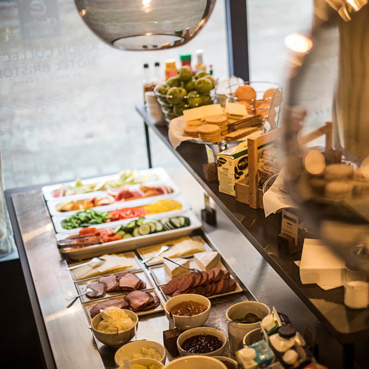 A breakfast buffet with various foods displayed on a counter, warmly lit within a restaurant.