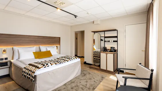 Moderni hotellihuone, jossa on mukava sänky, pieni minibaarialue ja viihtyisä nojatuoli.