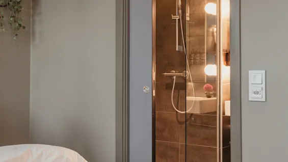 A comfortable bedroom with a view of a stylish bathroom featuring a glass shower and warm lighting.