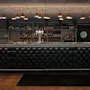 A stylish bar area with a black tufted counter, shelves stocked with bottles and glasses, and warm pendant lighting.