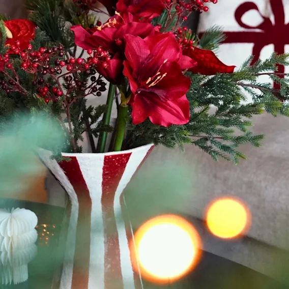 Röda julblommor i en vas och en mysig julkudde i soffan som sprider varm julstämning.
