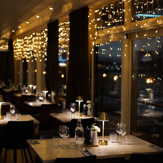 Mysig restauranginteriör med dukade bord och varma ljusslingor som hänger vid fönstren.