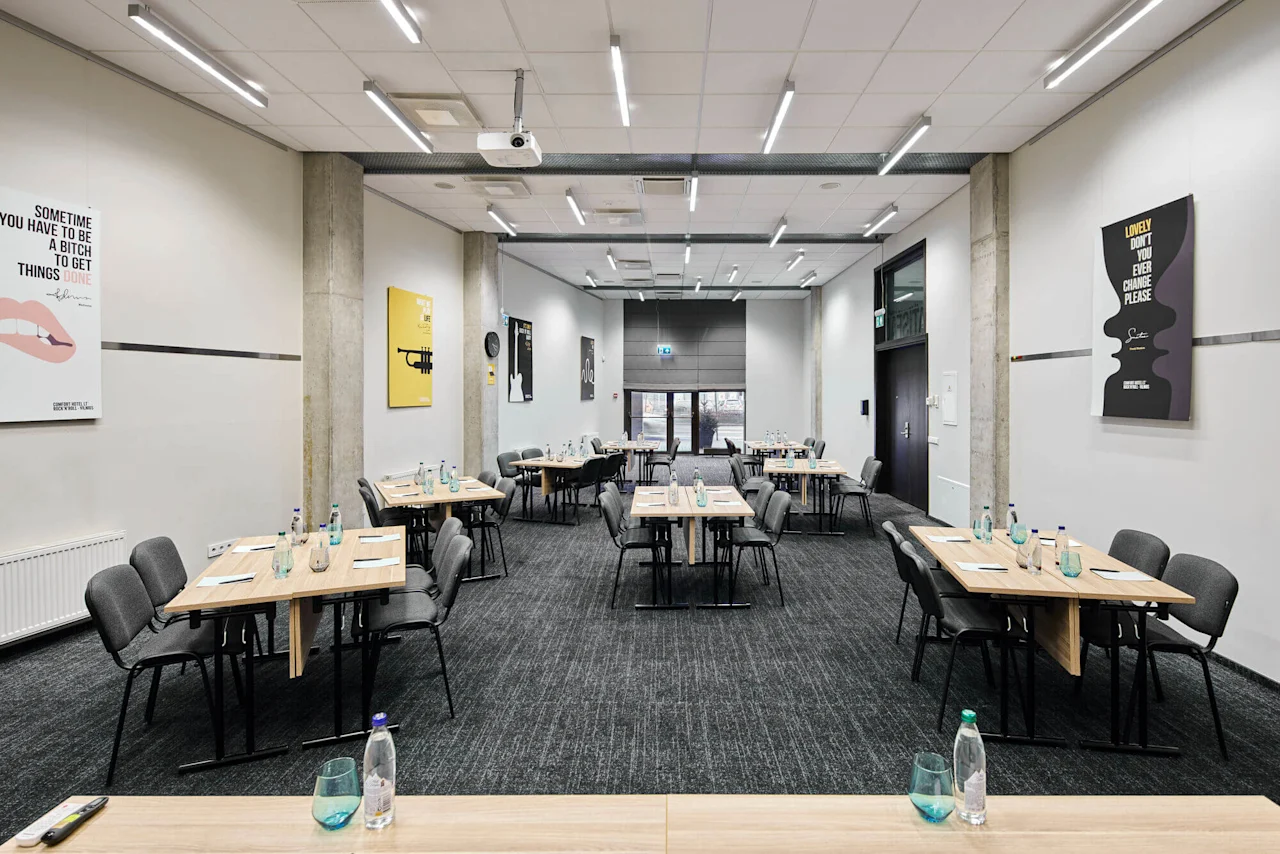Conference room with rectangular tables, chairs, and water bottles arranged for a meeting. Motivational posters on the walls include text like "SOMETIMES YOU HAVE TO BE A BITCH TO GET THINGS DONE."