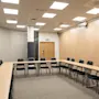 A spacious and well-lit conference room featuring a U-shaped table arrangement, light wood walls, and an exit sign.