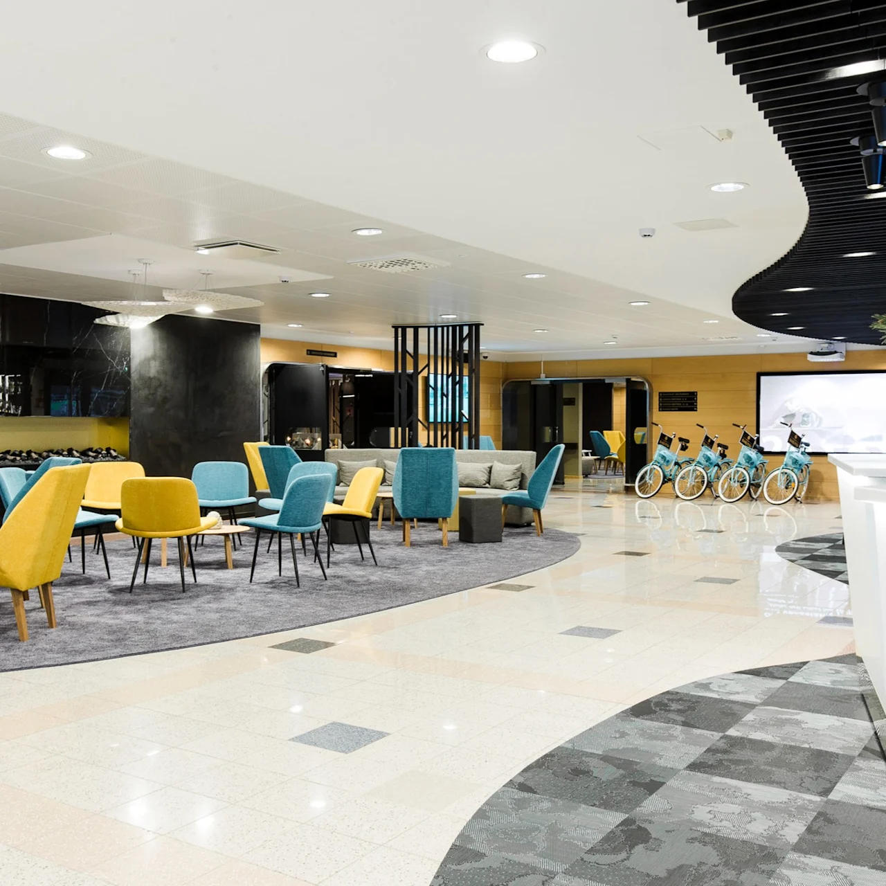 Elegant seating area with colorful chairs and sofas arranged for conversation, set in a modern lobby featuring a sleek black ceiling, bright lighting, and bicycles displayed in the background.
