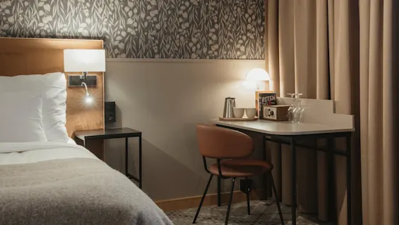 Ett mysigt hotellrum med säng och skrivbordsplats. På skrivbordet finns kaffeservis, vinglas och en bok ROTEN TILL.