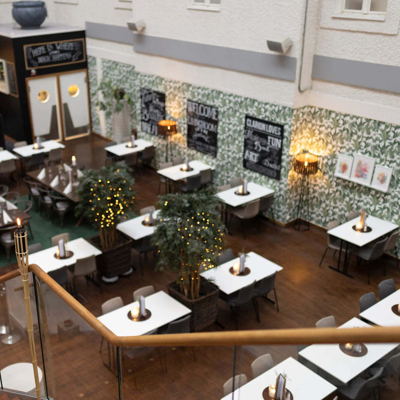 An elevated view of a restaurant interior with tables set for dining, warm lighting, and decorative greenery.