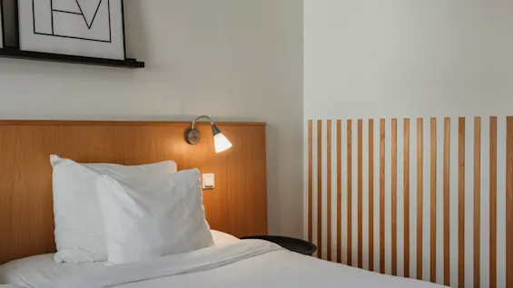 Viihtyisä hotellihuone Home Hotel Uppsalassa siististi pedatulla sängyllä, lämpimällä lukuvalolla ja modernilla puuseinäkoristeella.