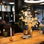 Et koselig spisebord med tørkede blader, rosa blomster, et tent lys og bøker i en dempet restaurant.