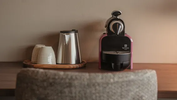 En kaffemaskin og vannkoker med kopper på et brett, klar for en varm drikke.