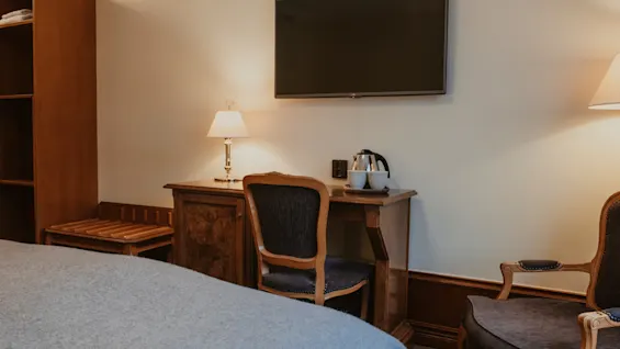 Ett bekvämt hotellrum med ett skrivbord, en TV ovanför, en stol och en säng, redo för gäster att koppla av eller arbeta.