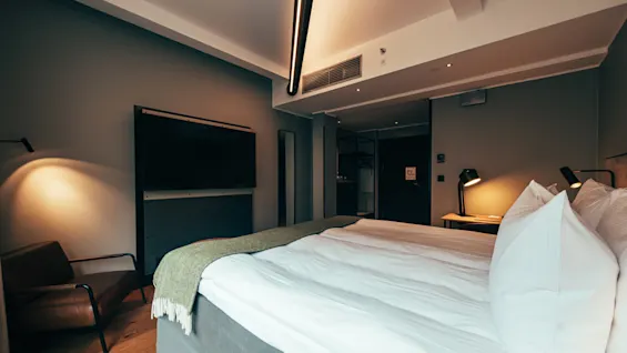 A cozy and modern hotel room with a comfortable bed, a large TV, and warm lighting, perfect for relaxation.