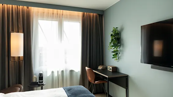 Et moderne og innbydende hotellrom med en komfortabel seng, et skrivebordsområde og en veggmontert TV.