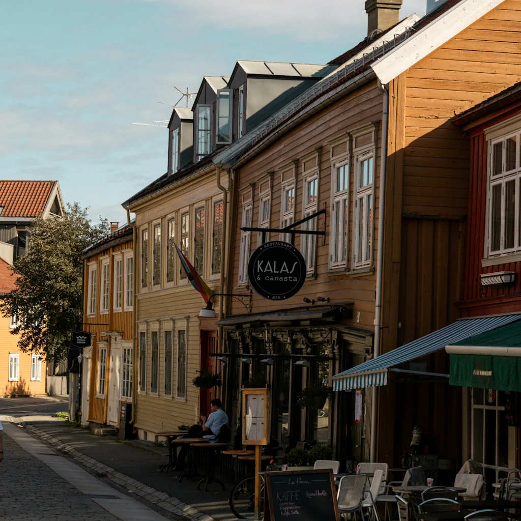 Viehättävä katunäkymä värikkäine puutaloineen ja ulkokahvilalla. Liitutaulu mainostaa Kaffe, Panini, Pizzaa.