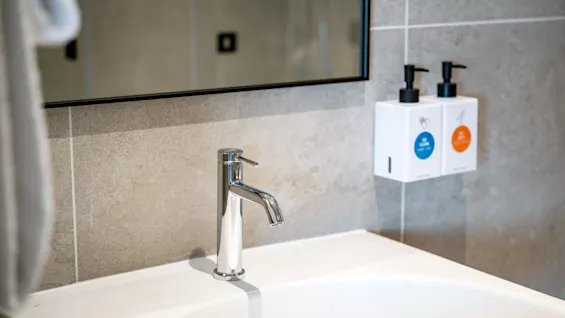 En ren, moderne baderomsvask med en kromkran, et speil og veggmonterte dispensere for håndhygiene.