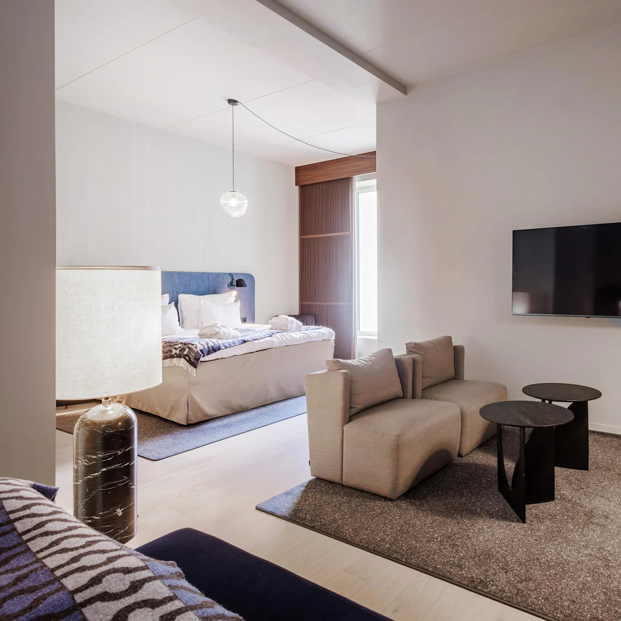 Modern living room with a beige sofa, adjacent bedroom area, art on walls, and a large floor lamp, illustrating a sleek interior.