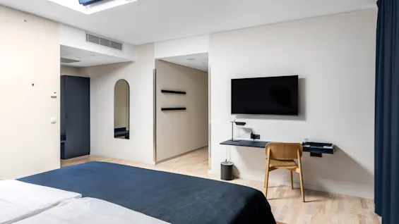 Et moderne hotelværelse med seng, skrivebord med TV og ovenlysvindue, i et rent og minimalistisk design.