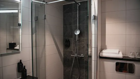 Et rent og moderne hotellbad med en glassdusj, speil og friske håndklær, klart for en forfriskende opplevelse.