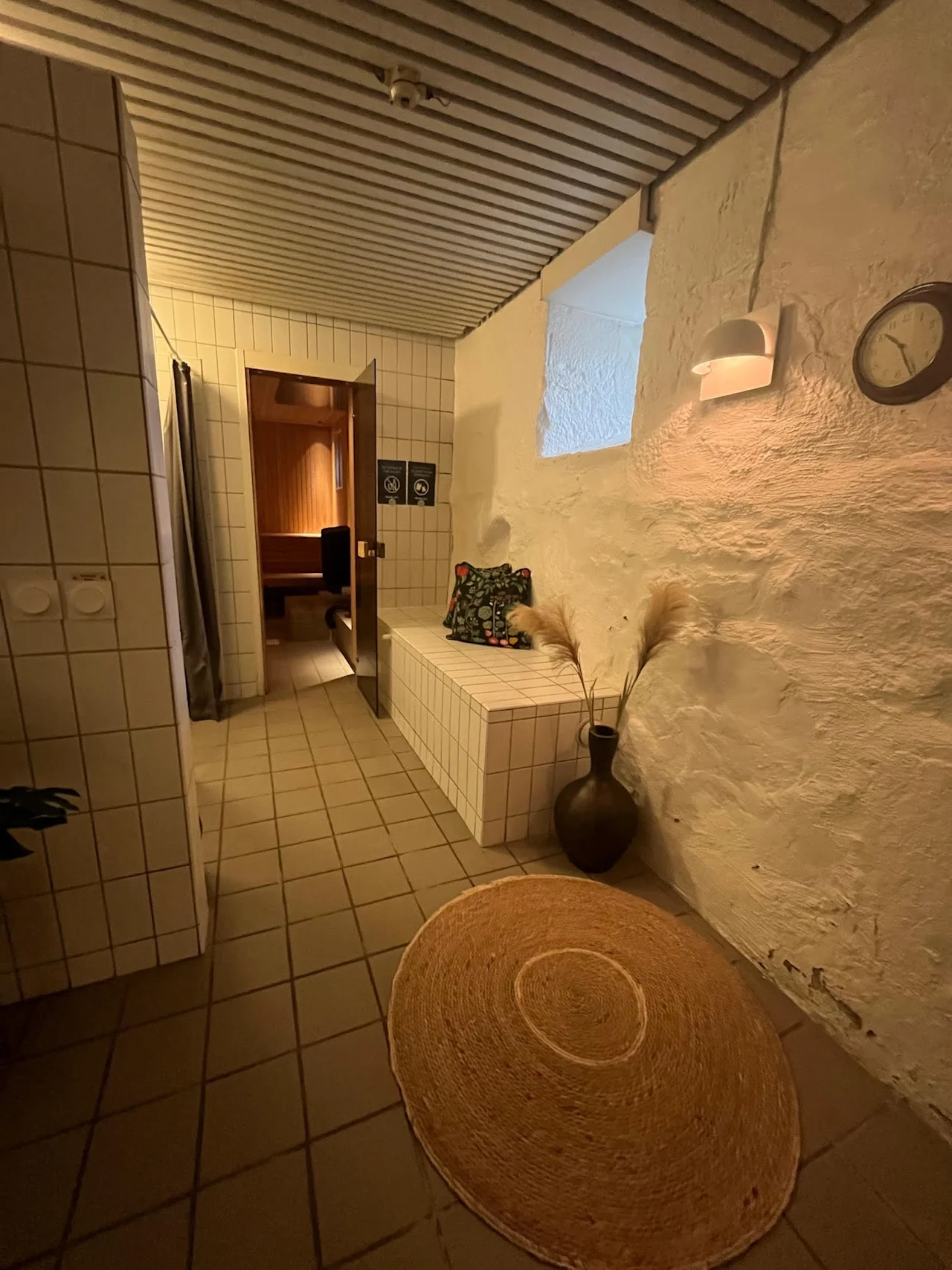 Innbydende velværested på Hotel Bilan, med badstueinngang, en komfortabel benk og varm belysning. To sirkulære symboler er på døren.