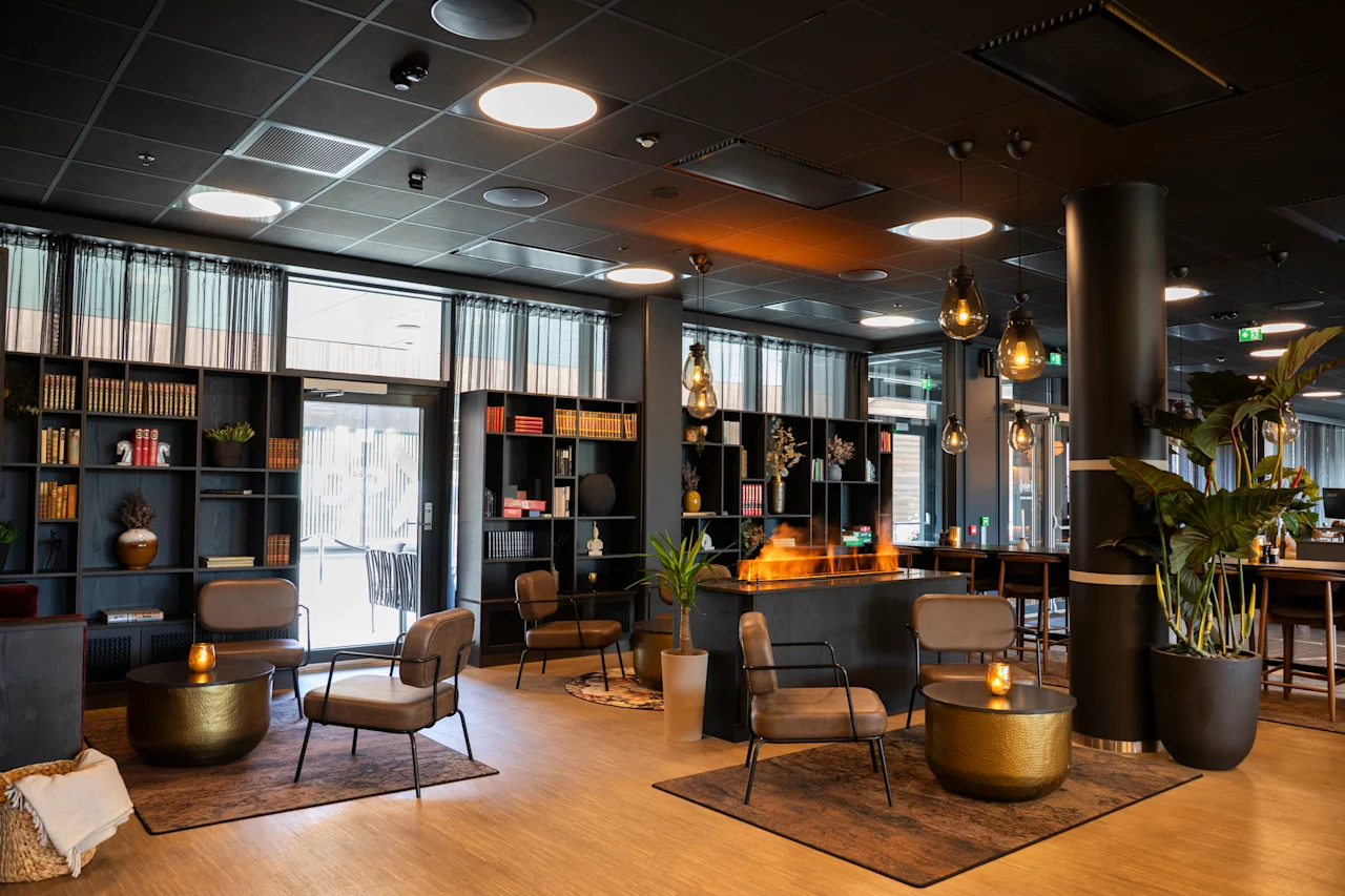En stilig hotellounge med moderne peis, bokhyller, komfortable stoler og store vinduer.