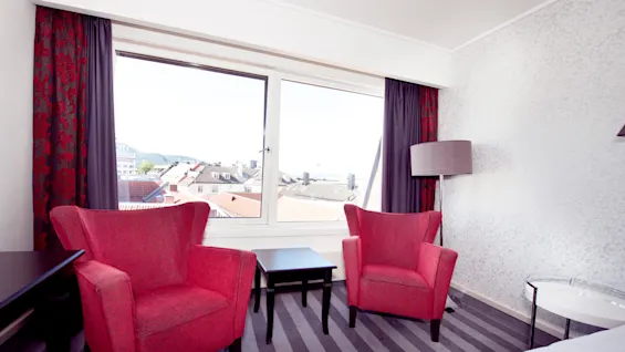 Two red upholstered chairs by a window with an open view of city rooftops in a bright, modern room.