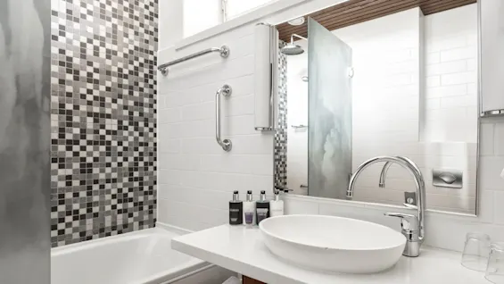 Modern bathroom with a white tub, basin on wooden vanity, and mosaic tiles. Bright interior with natural light and hygiene products.