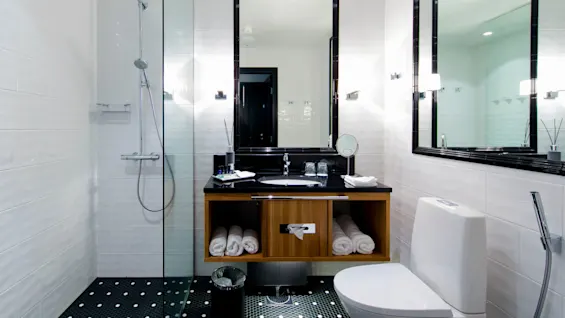 Et moderne bad med en brusekabine med glasvæg, en sort bordplade og en elegant toilet. Hvide fliser og spejle fremhæver det lyse, rene design.