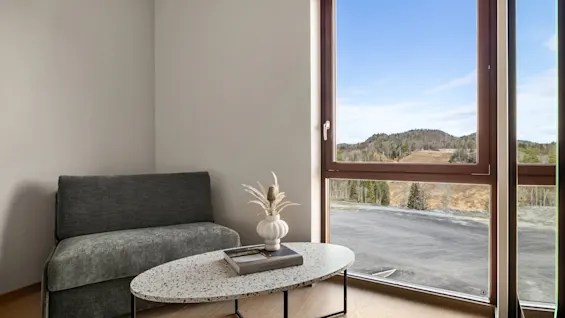 En koselig krok med sofa og salongbord, som tilbyr en naturskjønn utsikt over et fjellandskap gjennom et stort vindu.