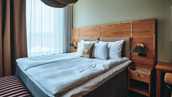 Et koselig hotellrom med en stor seng, sengegavl i tre og myk belysning, klart for et komfortabelt opphold.