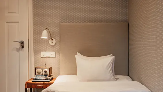 Et hyggeligt hotelværelse på Home Hotel Wellington med redt seng, sengebord med radio og bøger, samt væglampe.