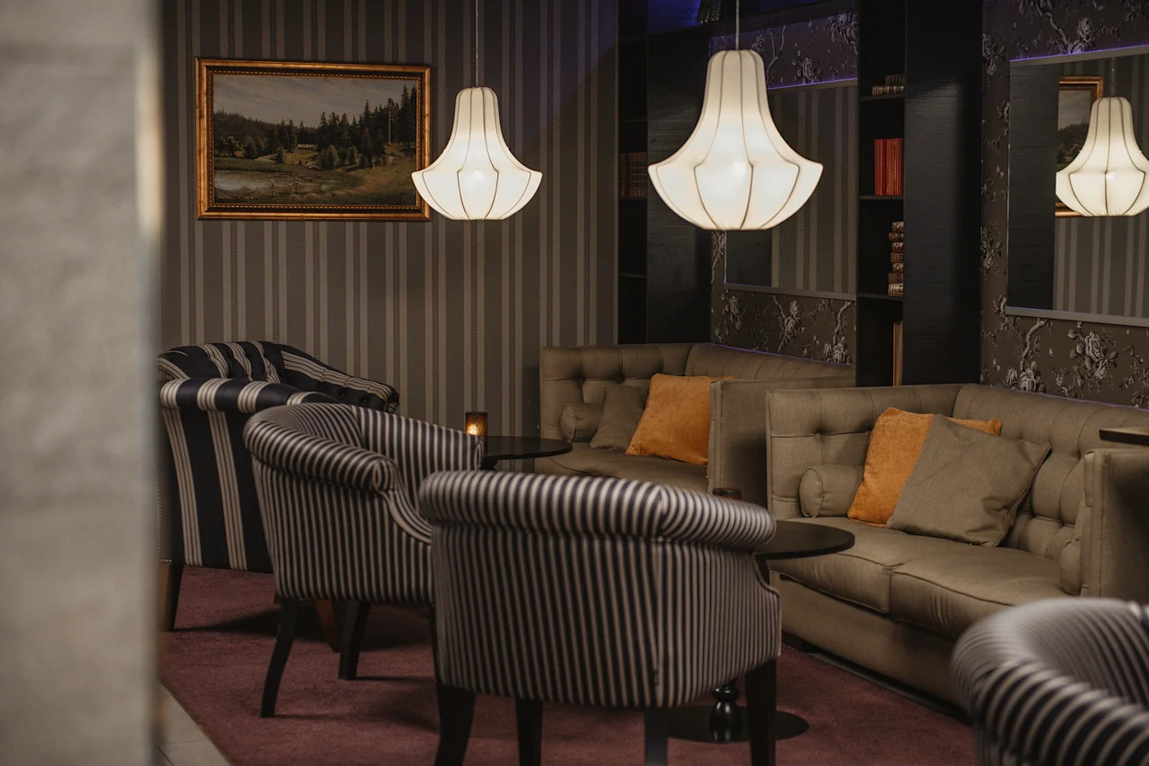 Viihtyisä hotellin oleskelutila, jossa on raidallisia nojatuoleja, mukava sohva ja tyylikkäitä riippuvalaisimia, täydellinen rentoutumiseen.