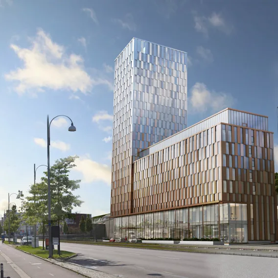 En hög, modern byggnad med reflekterande glaspaneler står på en stadsgata kantad med träd och gatubelysning. Nära finns en liknande glasbyggnad med texten "KPLASTIC" och "POC."