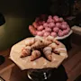 Vastaleivotut croissantit tomusokerilla pölytettynä telineellä, vaaleanpunaisten leivonnaisten kanssa taustalla.