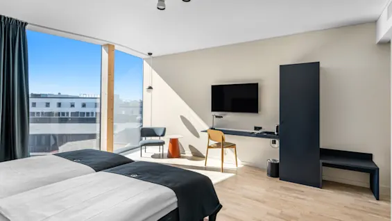Moderne hotelværelse med to enkeltsenge, stort vindue med udsigt over byen og et funktionelt skrivebordsområde.
