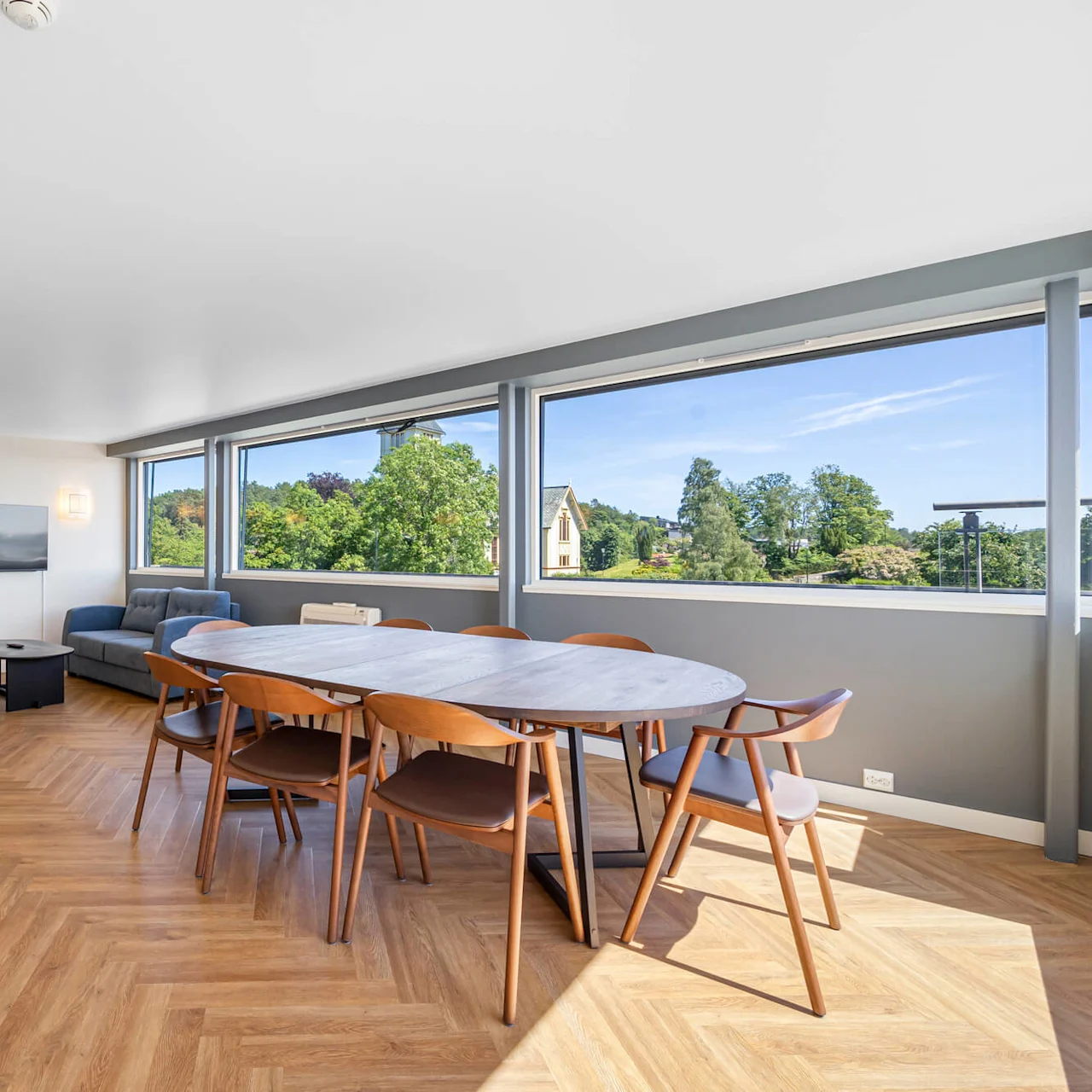 Bright, spacious hotel room with a dining area near large windows overlooking greenery, and an adjacent bedroom area.