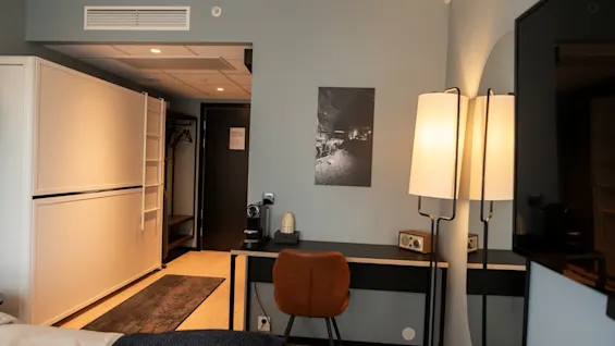 Et moderne hotellrom med en komfortabel seng, et funksjonelt skrivebordsområde med kaffemaskin og stilig belysning.