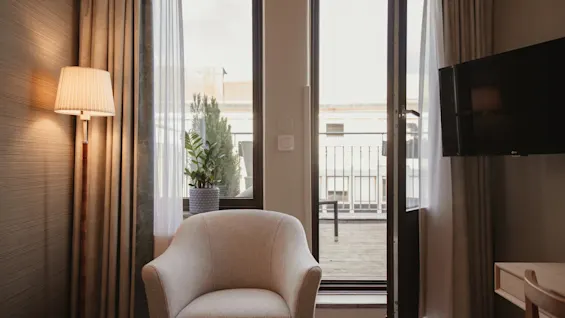 Et hyggeligt hotelværelse på Home Hotel Wellington med en komfortabel lænestol, en gulvlampe og en åben dør, der fører ud til en balkon.