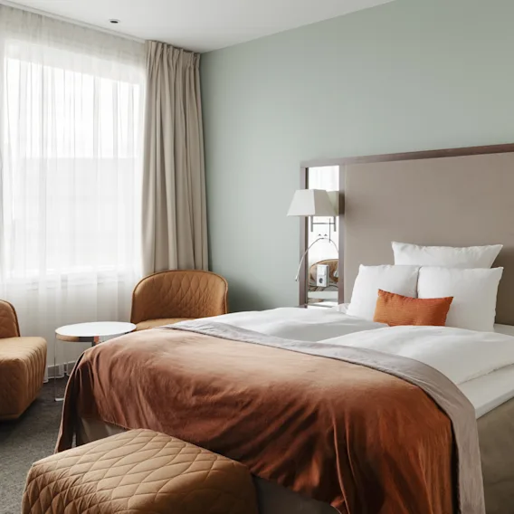 Ett mysigt hotellrum med en stor säng, två bekväma fåtöljer och mjuk belysning, perfekt för avkoppling.