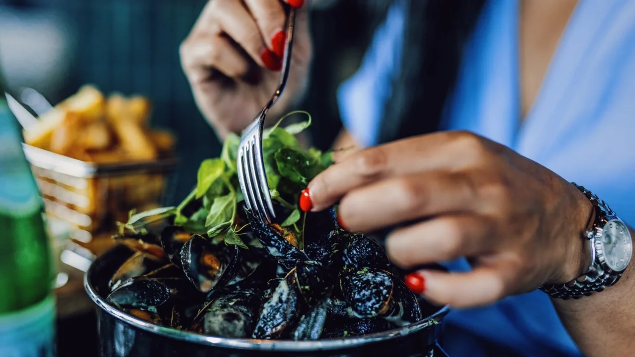 Woman eating mussles and fries at restaurant The Social Bistro & Bar.