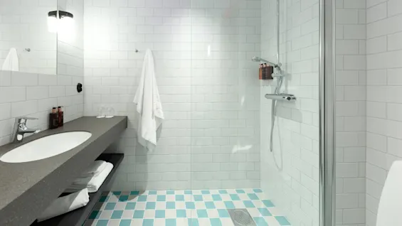A modern bathroom with white subway tiles, a glass shower, and teal-accented floor tiles.