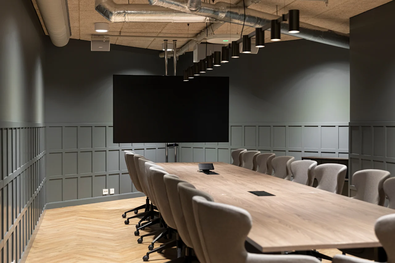 An empty, modern conference room with a large screen, a long wooden table, and many chairs, set for collaboration.