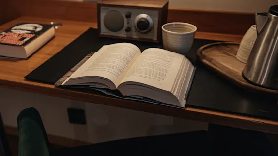 A cozy desk scene with an open book, a radio, and a kettle, inviting relaxation at Home Hotel Kung Oscar. 📚☕
