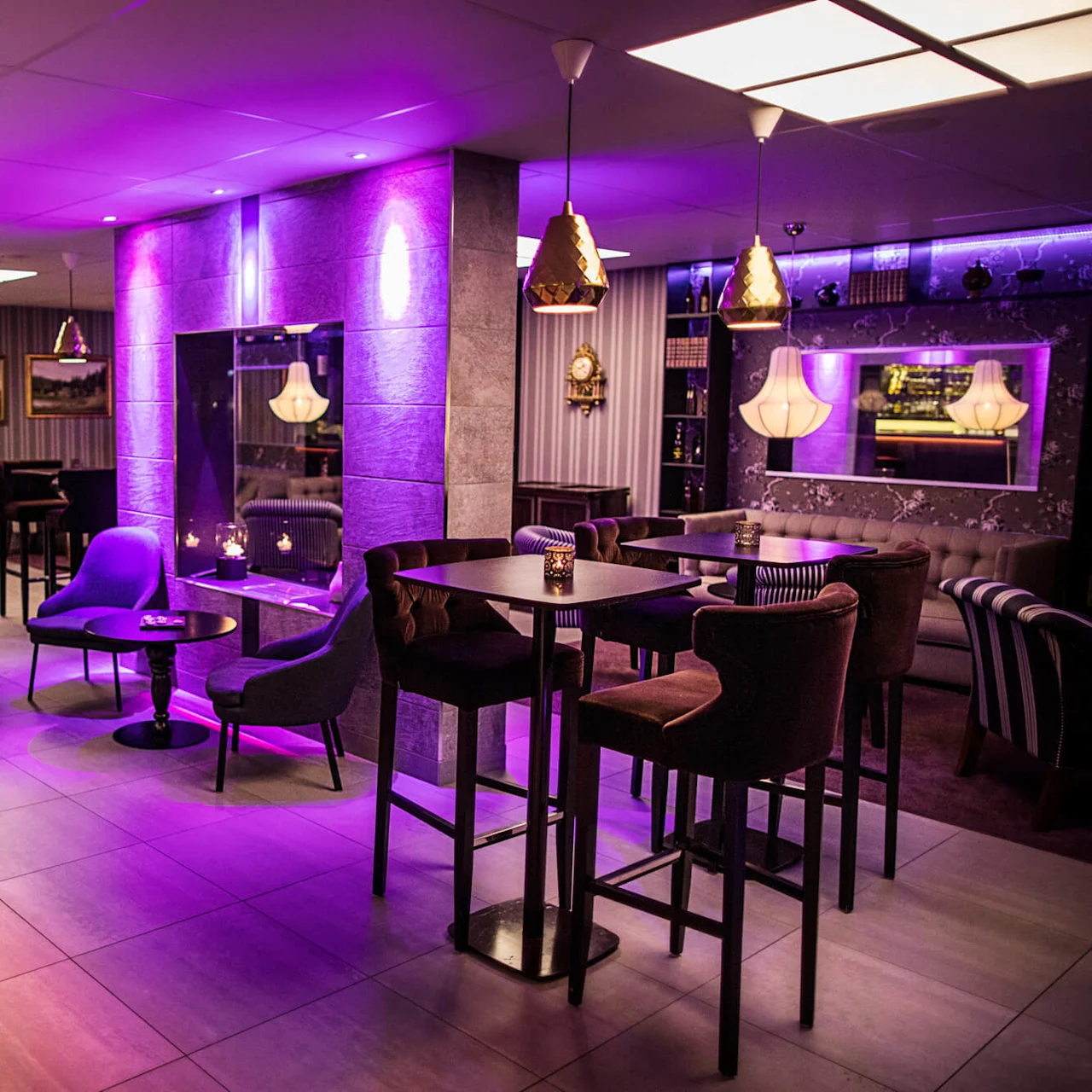 A cozy lounge area with purple lighting, comfortable chairs, and decorative candles, offering a warm, inviting ambiance.