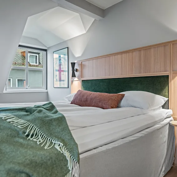 Et koselig hotellrom med en komfortabel seng, et grønt teppe og et vindu som gir et glimt av omverdenen.