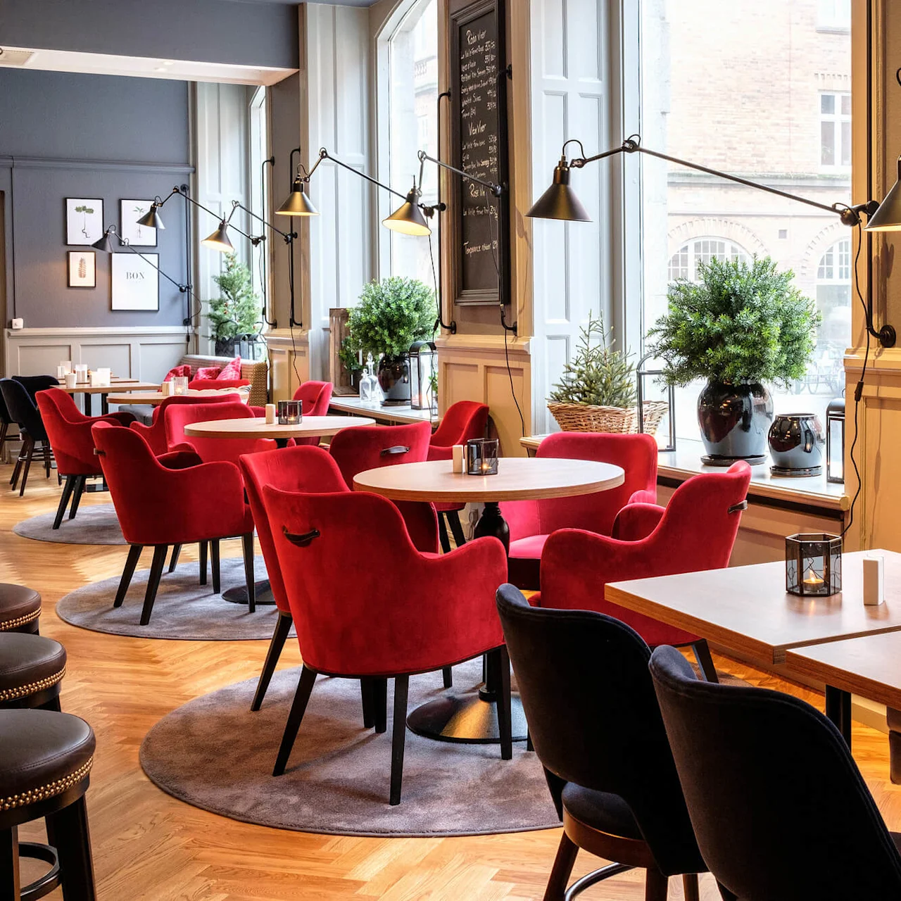 Red velvet chairs in an elegant cafe setting, with large windows and pendant lights.