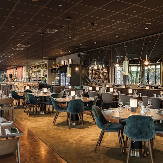 Elegant hotellrestaurang med mörkt tak, varm belysning och gröna sammetsstolar runt träbord.