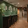 A modern hotel lobby with a long green counter and bar stools, framed art on the wall, and plants. Home Hotel Uppsala.