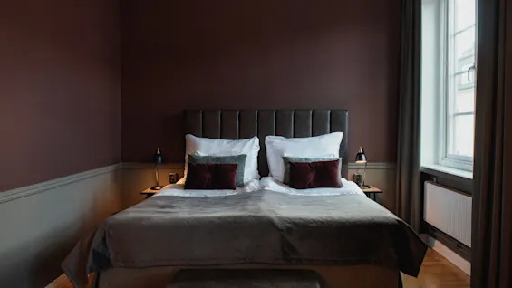 Viihtyisä hotellihuone, jossa on suuri sänky, tummat seinät ja valoisa ikkuna, kutsuen rentouttavaan oleskeluun.