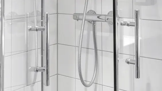 A showerhead and controls mounted on a tiled wall inside a glass-door shower enclosure.
